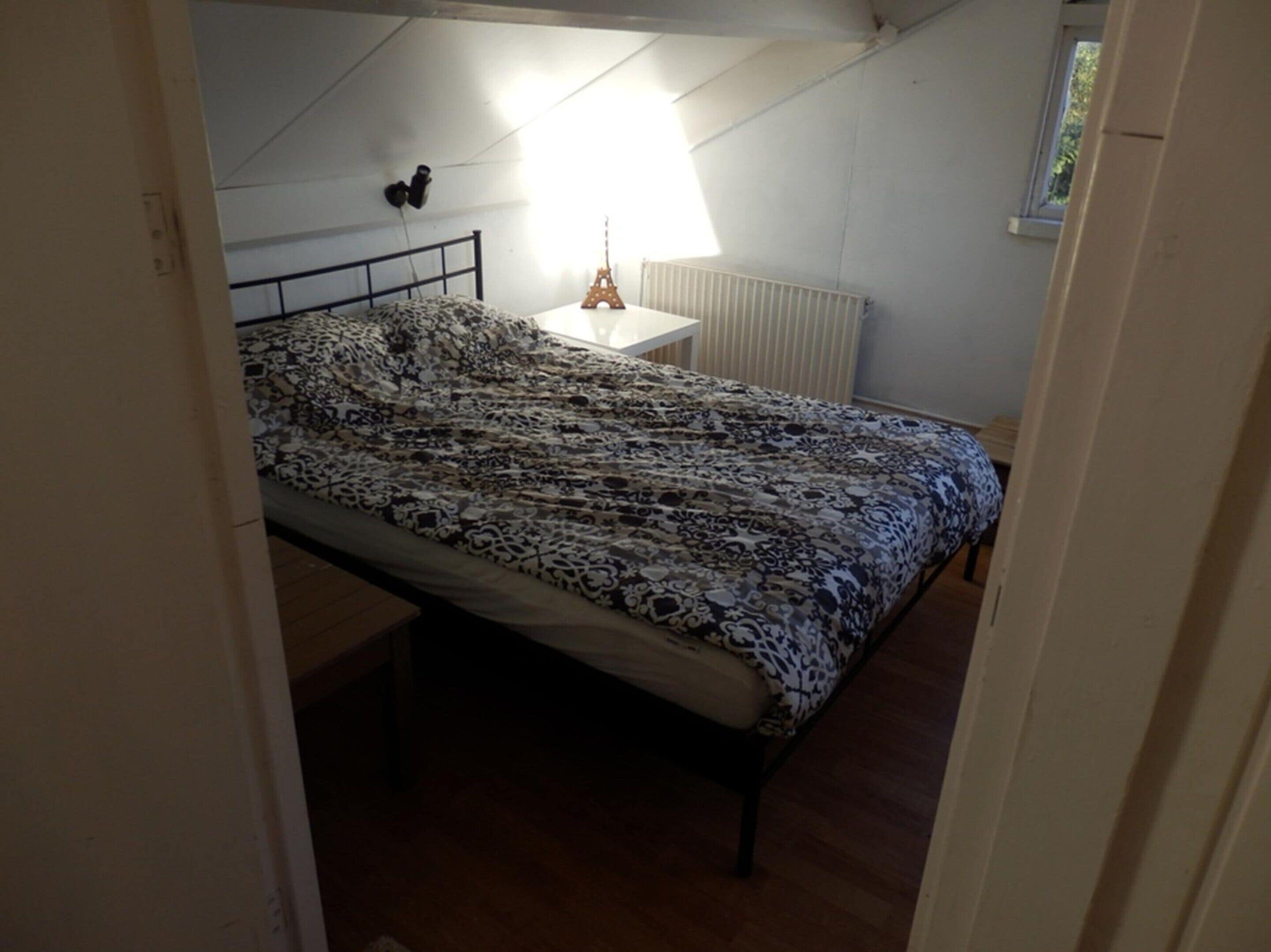 A bedroom with a bed, a nightstand, a radiator, and a window.