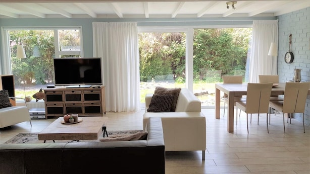 Uma sala de estar moderna com televisão de tela plana, um sofá, uma mesa de centro e uma área de jantar com cadeiras e uma mesa.