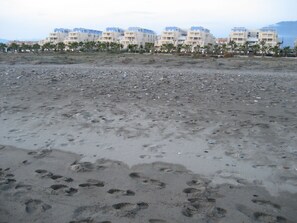A sandy beach with footprints, palm trees, and a row of buildings in the background. - Two-story penthouse right on the beach. Dream Subdivision (AN)