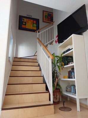 A staircase with a wooden handrail and beige steps, leading to a landing with a television and a bookshelf. - Two-story penthouse right on the beach. Dream Subdivision (AN)