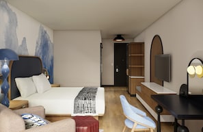 Moderni hotellihuone, jossa on sänky, työpöytä, tuoli, televisio ja kirjahylly.