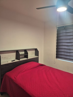 A bedroom with a bed, a ceiling fan, and a window with blinds.