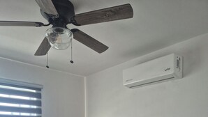 Een slaapkamer met een bed, een plafondventilator, een airconditioningapparaat, een raam met jaloezieën en een inbouwkast.