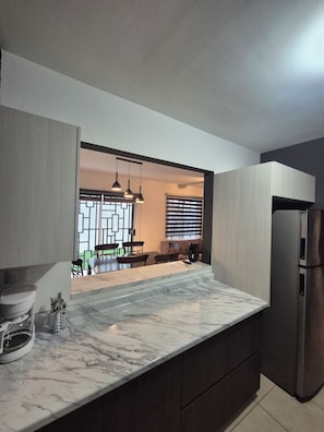 A modern kitchen with a marble countertop, built-in appliances, and a view into the dining area.