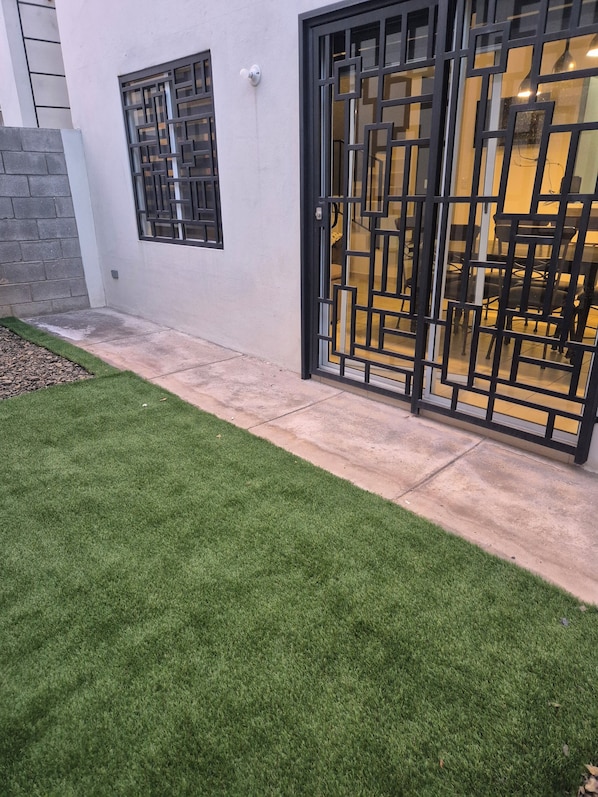 A modern building exterior with a well-maintained lawn, a black metal gate, and a visible interior with a dining area.