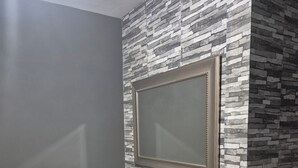Een badkamer met een grijze muur, een accentmuur met een steenmotief, een donker houten wastafelmeubel, een spiegel en een potplant.
