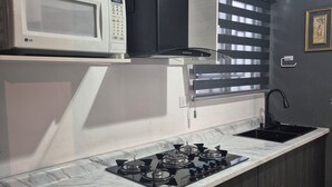 Een keuken met een ingebouwde magnetron, een gasfornuis en een raam met zonwering.