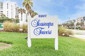 A sign for Seascape Towers with the number 5207, surrounded by grass and palm trees. - 🏖️ Seascape Towers 1025 | Direct Oceanfront Condo | Balcony + Pool Access (New Smyrna Beach)