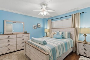 A bedroom with a bed, a dresser, a mirror, a ceiling fan, and a window with curtains. - 🏖️ Seascape Towers 1025 | Direct Oceanfront Condo | Balcony + Pool Access (New Smyrna Beach)