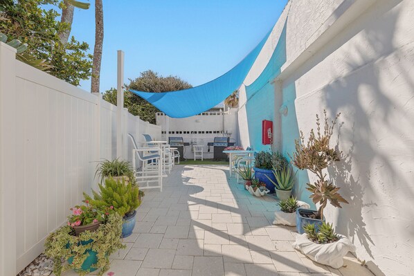 A patio area with outdoor furniture, potted plants, and a blue shade sail. - 🏖️ Seascape Towers 1025 | Direct Oceanfront Condo | Balcony + Pool Access (New Smyrna Beach)