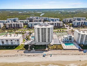 A high-rise hotel with multiple floors, a rooftop pool, and a beach area with umbrellas. - 🏖️ Seascape Towers 1025 | Direct Oceanfront Condo | Balcony + Pool Access (New Smyrna Beach)