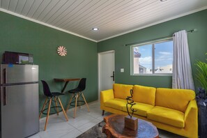 Ein Wohnzimmer mit gelbem Sofa, zwei Sessel, einem Holztisch und einem dekorativen Wandelement.