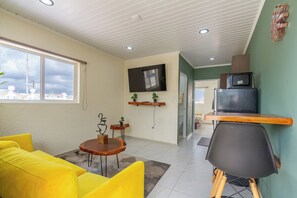 En moderne stue med en sofa, et rundt bord og et fjernsyn ophængt på væggen.