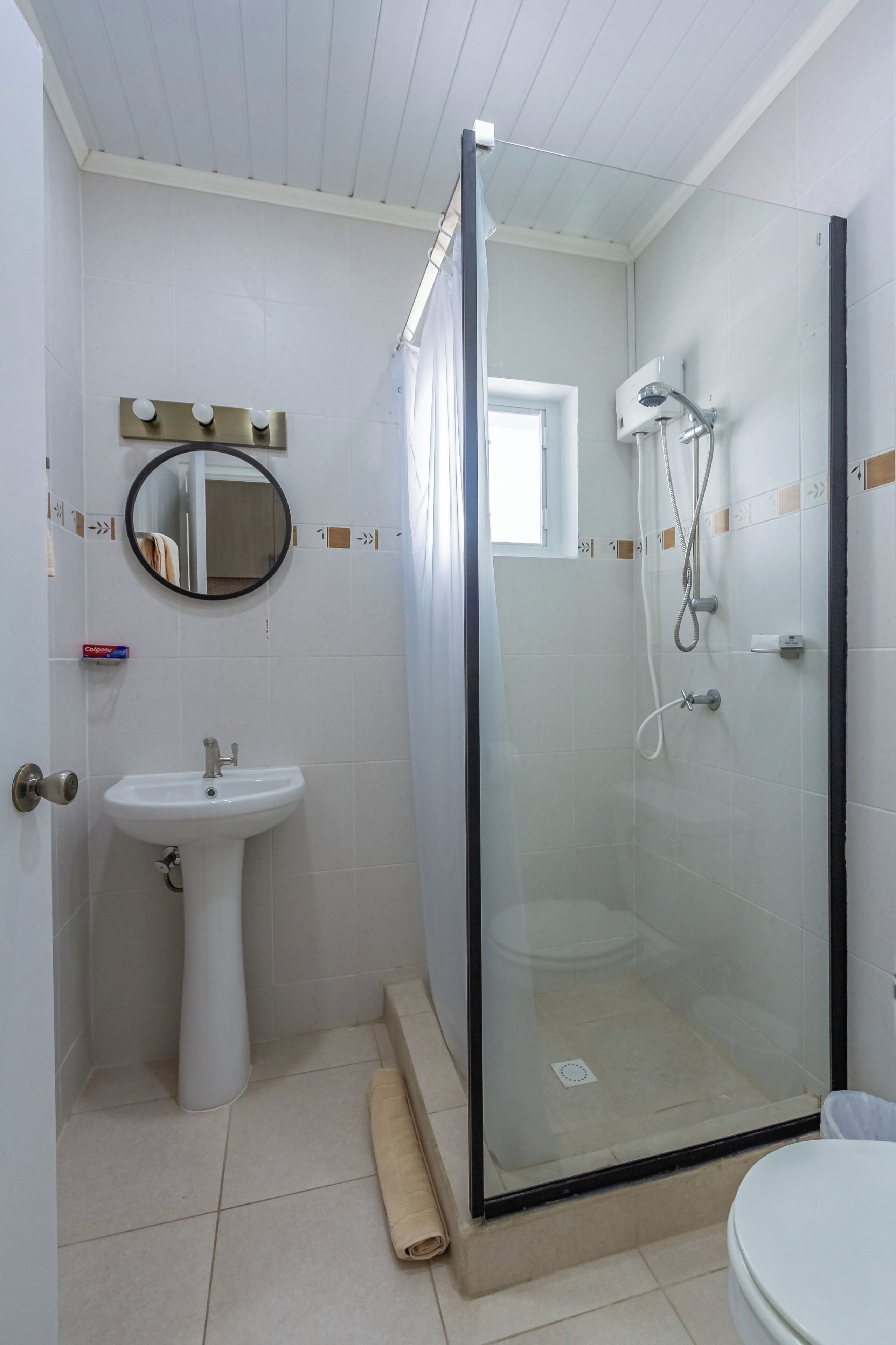 A bathroom with a glass-enclosed shower, a pedestal sink, and a mirror.