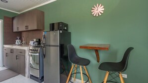 A compact kitchen with a refrigerator, stove, and microwave. There are two black chairs and a small wooden table. - Aruba Vibe Apartments #1 | Charming Studio Near the Beaches and Downtown (Oranjestad)