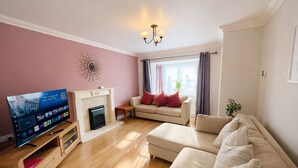 Ein Wohnzimmer mit Fernseher, einer Couch, einem Kamin und einem Wandbild.
