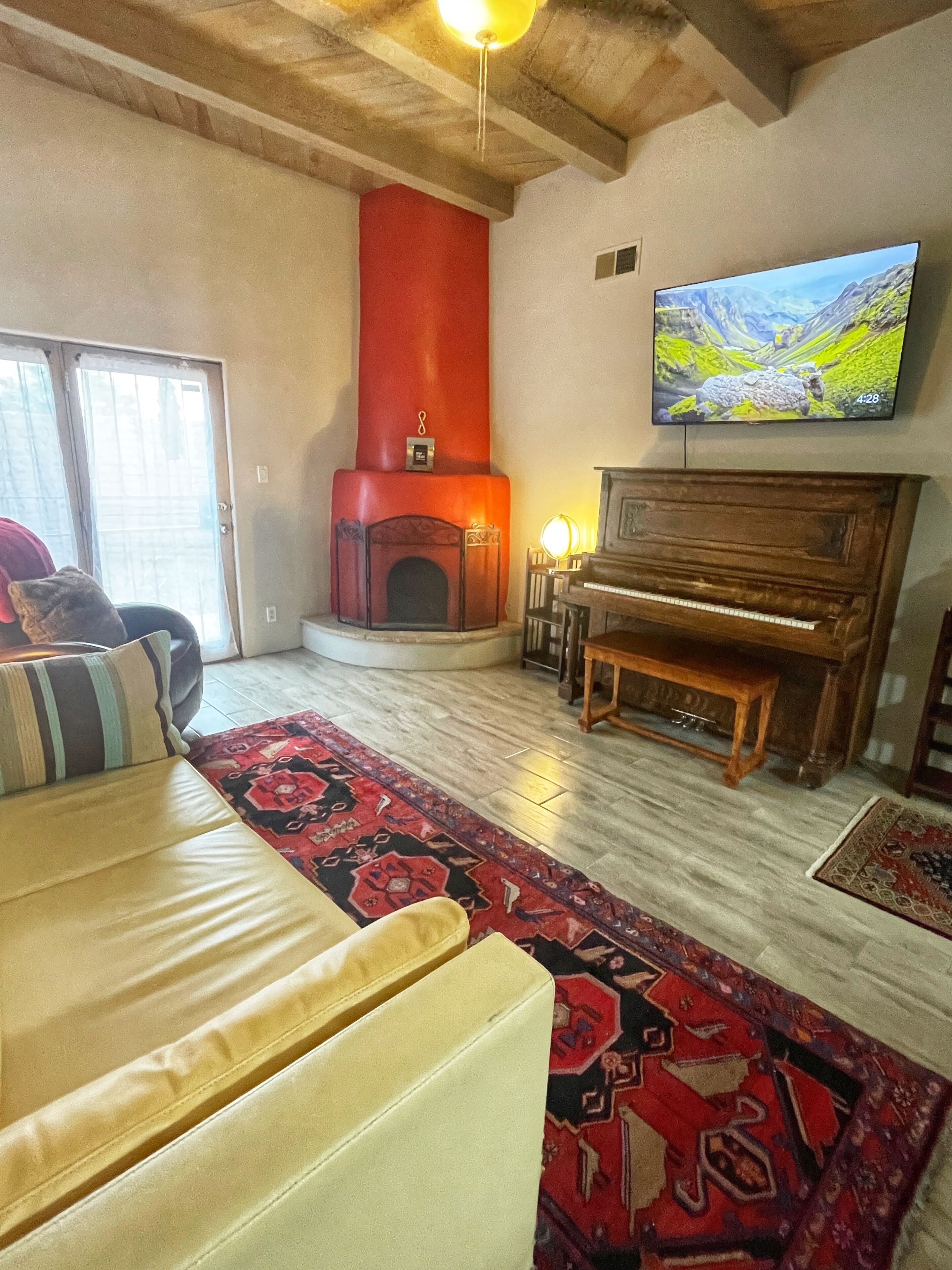 Una sala de estar con chimenea, un televisor montado en la pared, un piano y un sofá con cojines estampados.