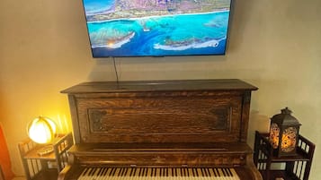 A wooden piano with a bench, a television mounted on the wall, and two wall-mounted lamps.