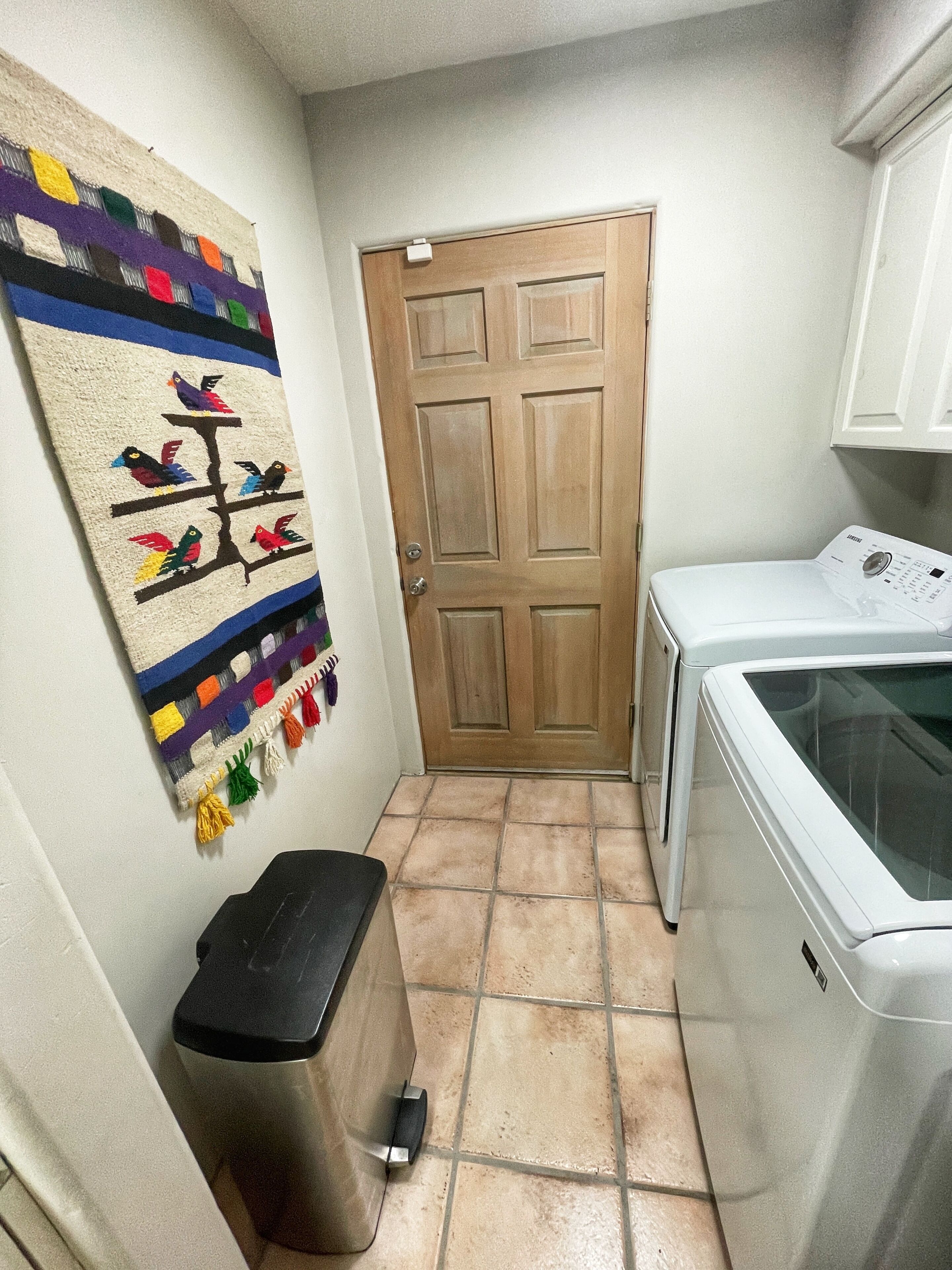 A laundry room with a washing machine, a door, and a trash bin.