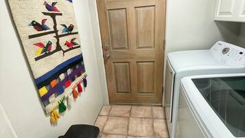 A laundry room with a washing machine, a door, and a trash bin.