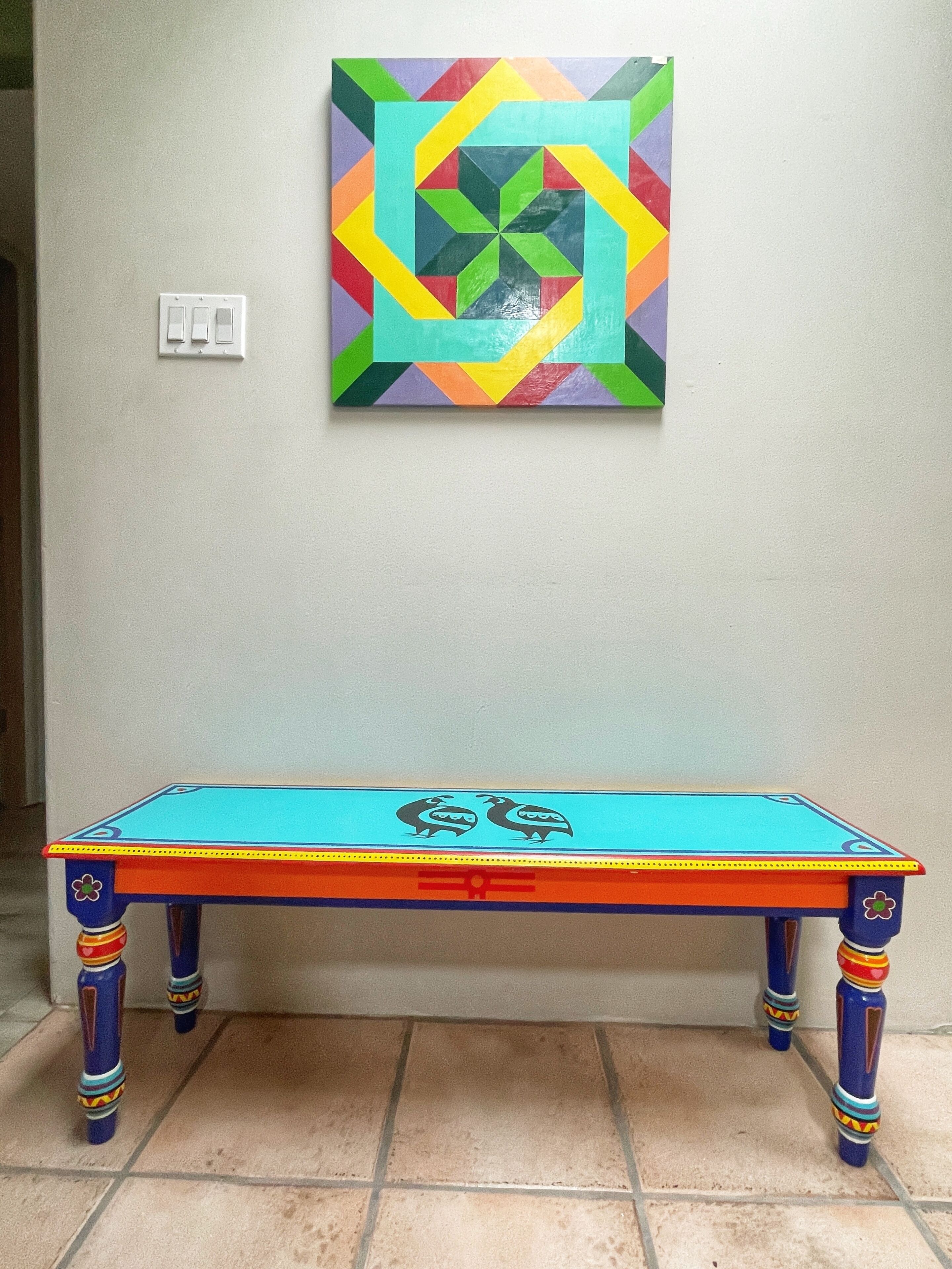 A table with a colorful geometric design on the tabletop and a wall-mounted artwork above it.