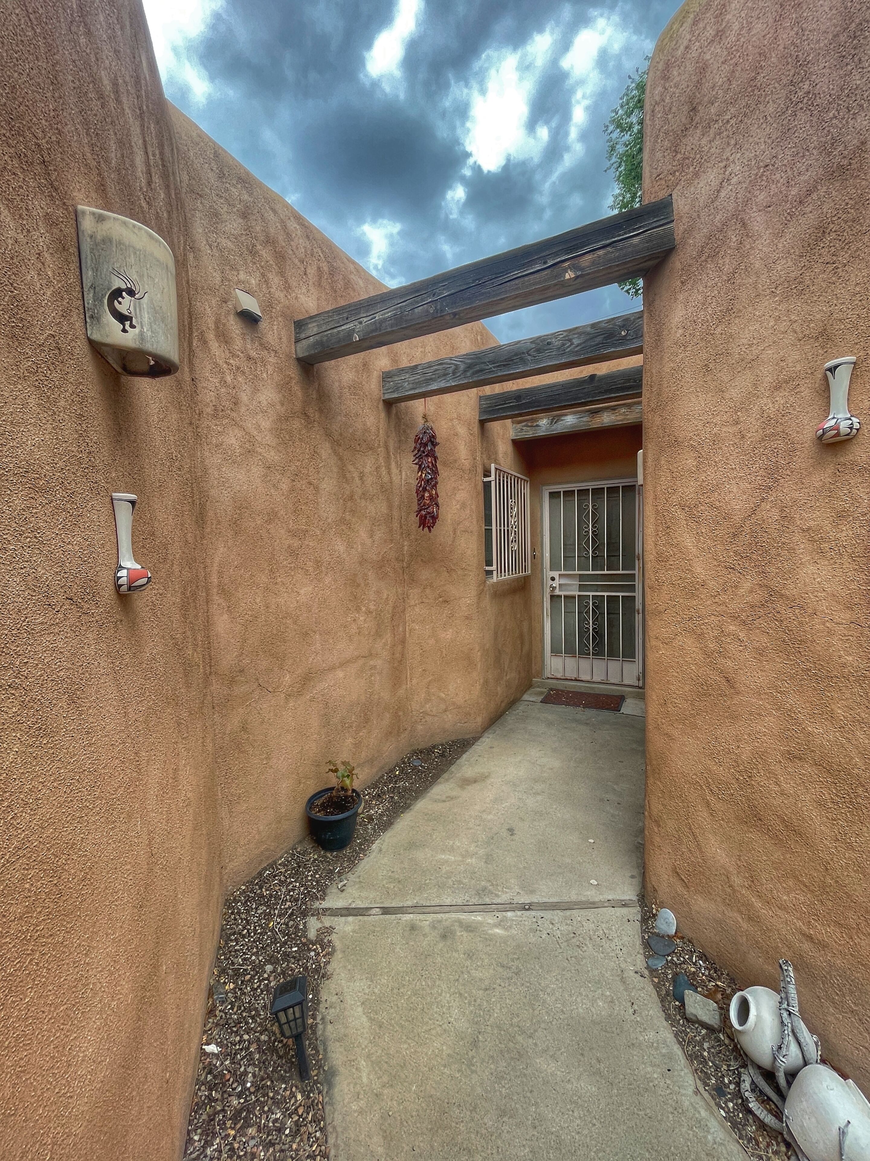 A narrow outdoor corridor with textured walls, a potted plant, and a metal gate.