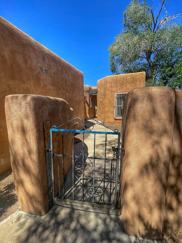 Una entrada con portón metálico y un camino de concreto que conduce a un patio con edificios.