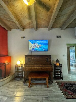 Una habitación con techo de madera, un televisor en la pared, un piano y una chimenea.