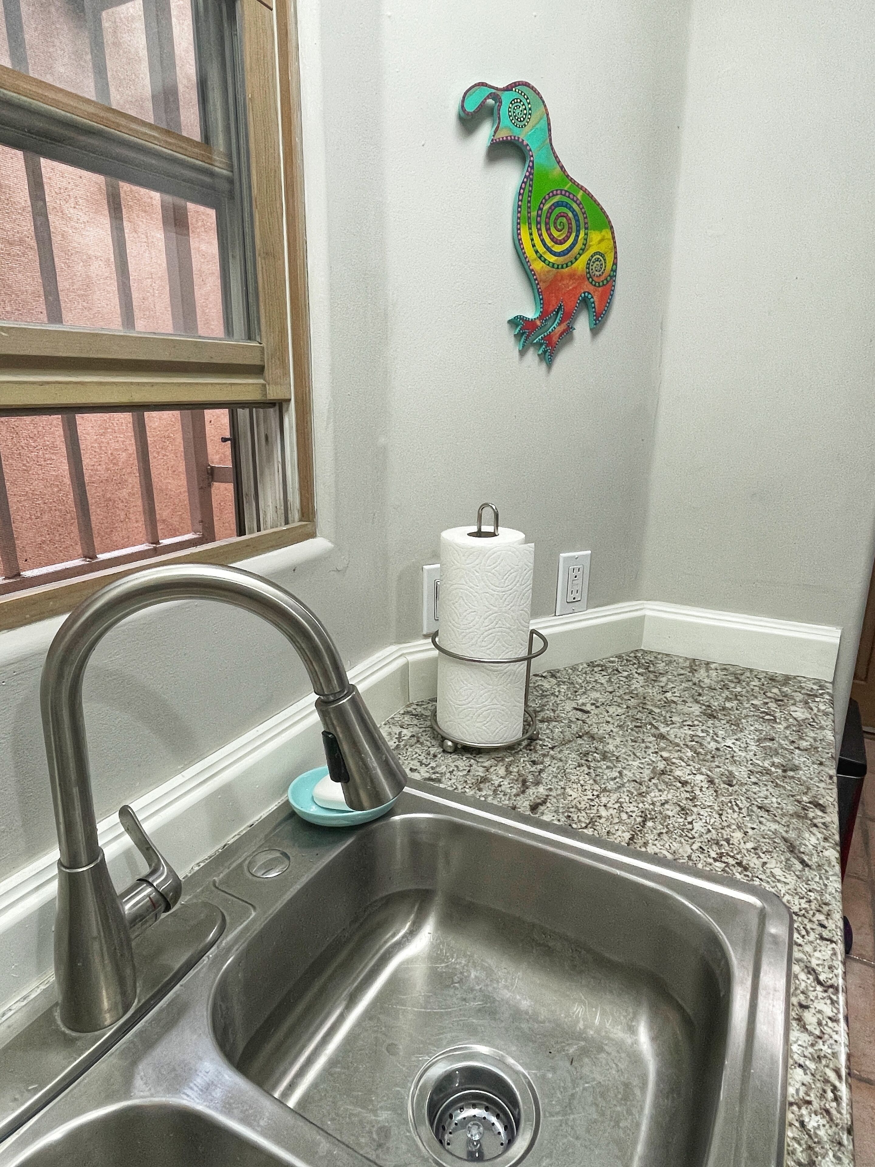 Una cocina con un lavamanos de acero inoxidable, una ventana con rejas y una decoración de pared colorida.