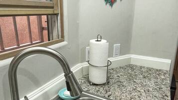 Una cocina con un lavamanos de acero inoxidable, una ventana con rejas y una decoración de pared colorida.