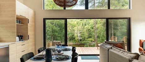 Une cuisine moderne avec un coin repas, de grandes fenêtres et une vue sur l’extérieur.