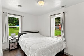 A bedroom with a bed, a nightstand, a lamp, and two windows with curtains. - Andover Retreat • Near Hiking & Boating (Andover)