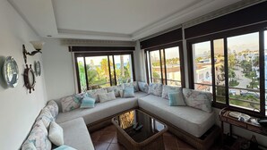 A spacious living room with a large sectional sofa, a coffee table, and a view of a coastal area. - Mediterranean Getaway (Fnideq)