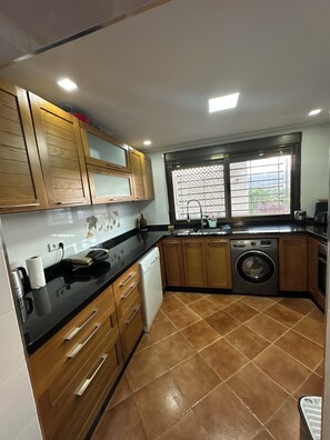 A kitchen with wooden cabinets, a washing machine, and a window with a view. - Mediterranean Getaway (Fnideq)