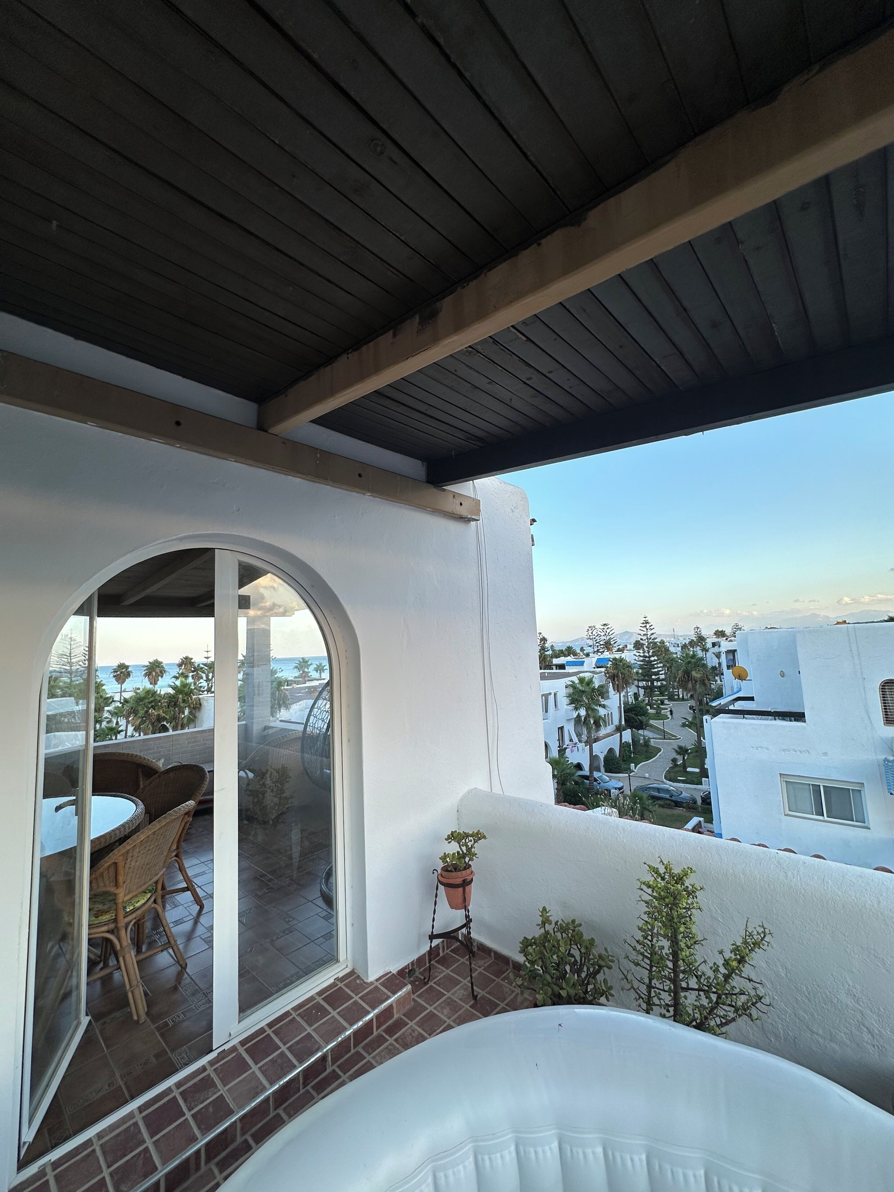 Un balcó amb vista al mar, una taula de vimet i una planta en test.
