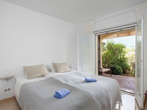 Une chambre à coucher avec un lit, des oreillers, une table de chevet et une vue sur un jardin, visible à travers une porte ouverte.