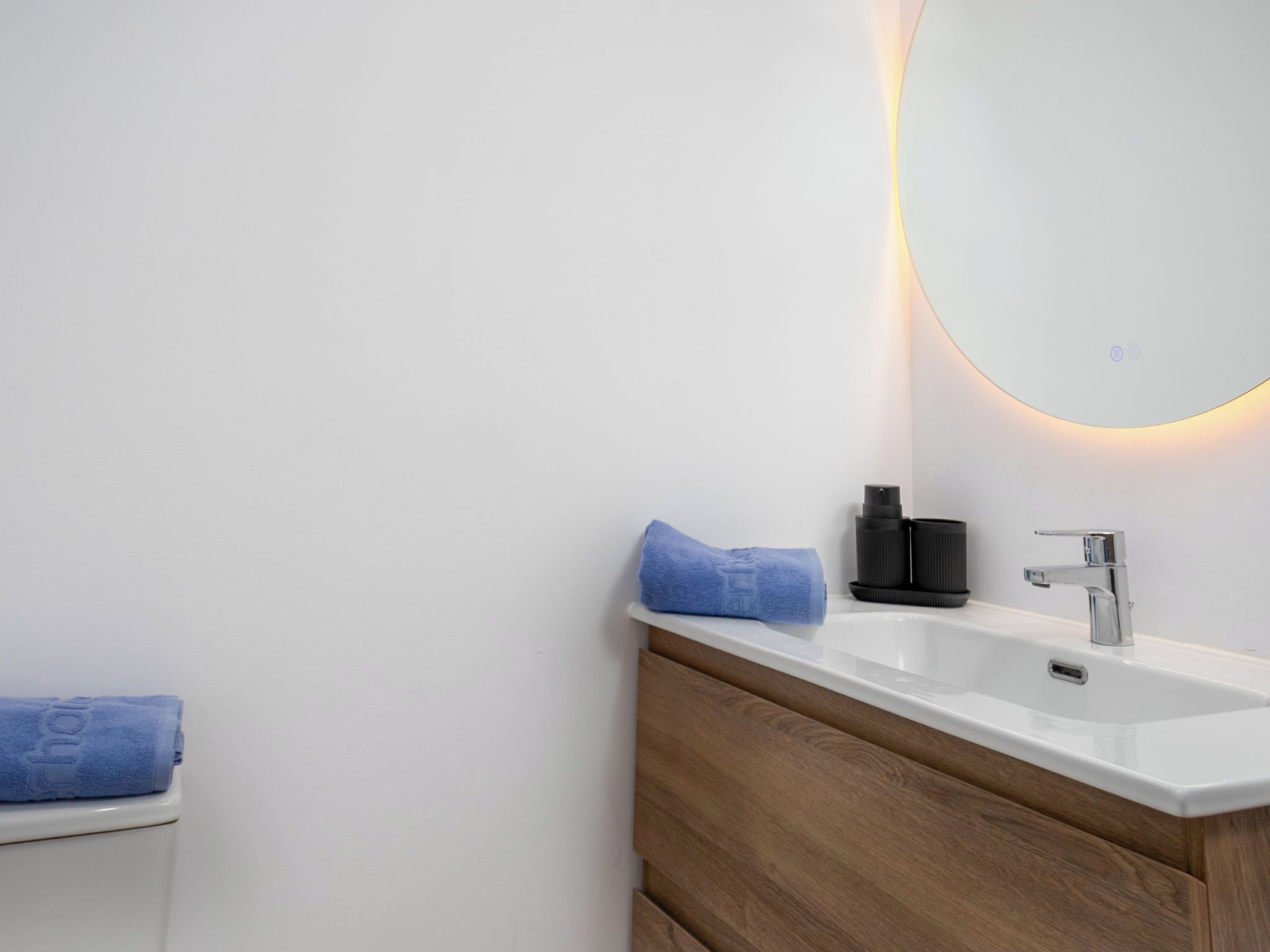 A bathroom with a white sink, a mirror with a light, and a towel on the counter.