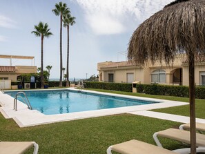 Une piscine avec des chaises longues, des palmiers et un bâtiment doté d’un toit en tuiles.