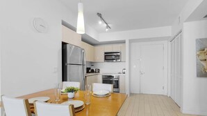 A modern kitchen with stainless steel appliances, a dining table with chairs, and a clock on the wall. - Sunset Views 2BR - 2BTH w/ Bay View Fitness Center (Hallandale Beach)