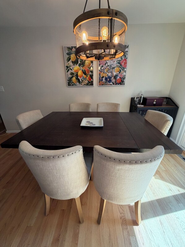 Uma área de jantar com uma mesa de madeira escura, seis cadeiras e um lustre.