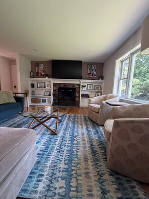 Ein Wohnzimmer mit Kamin, einem blauen Teppich mit Muster und einem großen Fenster.