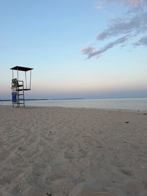 Uma praia com uma cadeira de salva-vidas e uma placa, céu claro e mar calmo.
