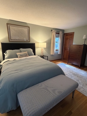 A bedroom with a bed, bedside lamp, wooden wardrobe, and a bench. - Peaceful 3-bedroom house in quaint Barnstable neighborhood near Craigville Beach (Barnstable)