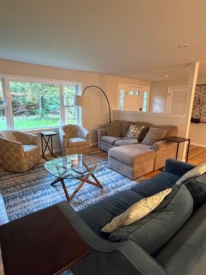 A living room with a sofa, armchair, and a glass coffee table. - Peaceful 3-bedroom house in quaint Barnstable neighborhood near Craigville Beach (Barnstable)