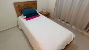 A single bed with a wooden headboard, a nightstand, and a curtain on the window.