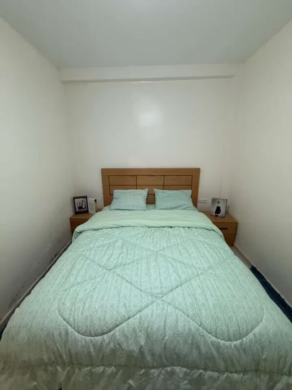 A single bed with a wooden headboard in a room with plain walls.