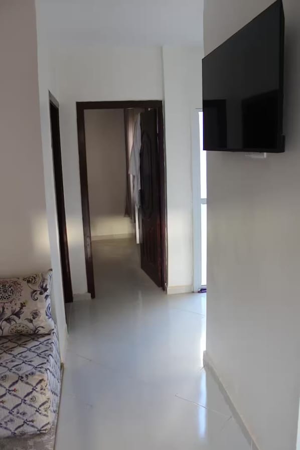 A hallway with a flat-screen TV mounted on the wall, leading to a room with a patterned sofa.