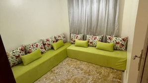 A room with a green sofa set, a patterned rug, and a ceiling light fixture.