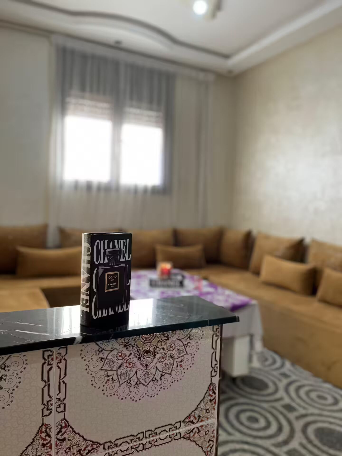 A living room with a sofa, a coffee table, and a book titled 'CHANEL' on a stand.