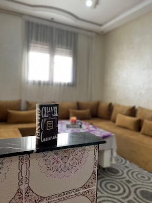Een woonkamer met een bank, een salontafel en een boek met de titel 'CHANEL' op een standaard.